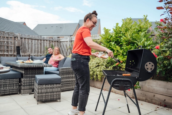 Ein Mensch legt mit einer Grillzange Würstchen auf einen Grill.